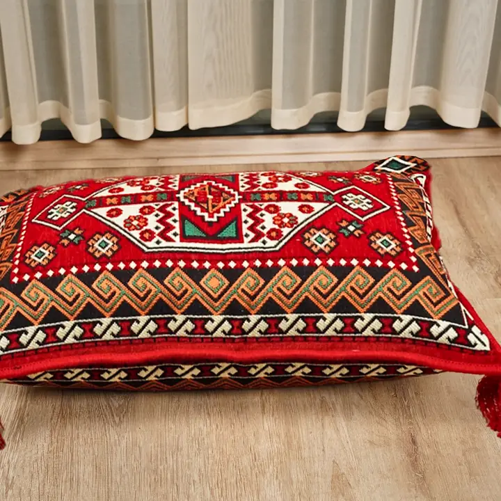 Single red floor pillow in a geometric weave with tassels at each corner, set on its own on a wooden floor