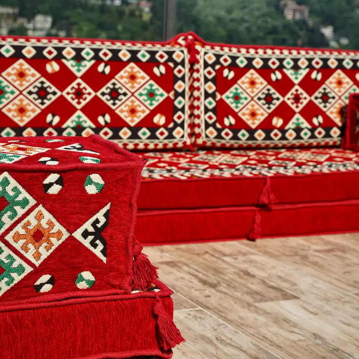 Red kilim-pattern floor sofa seen close up, with a seat built from two stacked layers, patterned backrests and a square ottoman in front