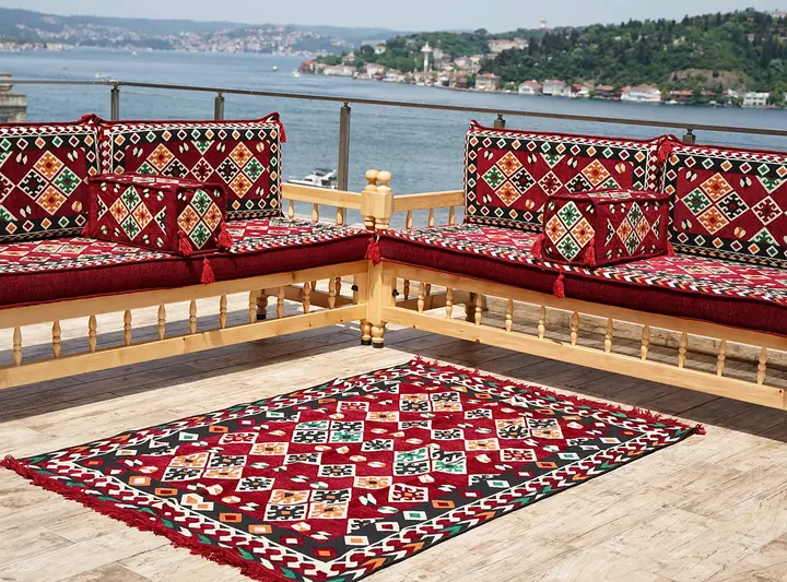 Two wooden benches meeting at a corner in an L, with red diamond kilim cushions, cube pillows and a matching kilim rug