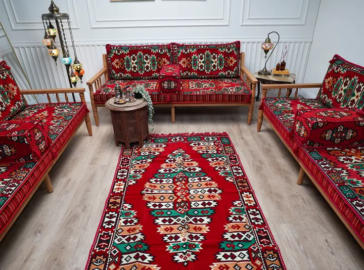 Red kilim cushions on pine benches facing each other across a long red runner rug, with a carved side table and hanging mosaic lamps