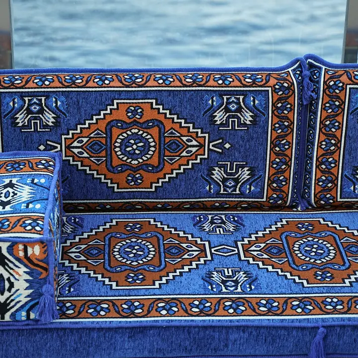 Close front view of a royal blue medallion floor sofa with a patterned armrest bolster at the end of the seat