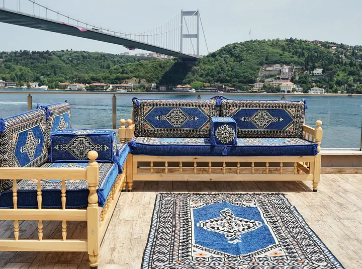 Two pine benches with royal blue medallion cushions set in an L beside a blue medallion kilim rug on a terrace by the water