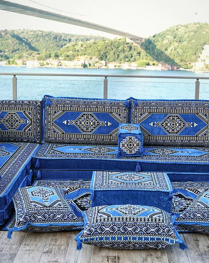 Royal blue floor seating wrapping three sides of a sunny terrace, with diamond-medallion backrests, double-layer seats and a square ottoman