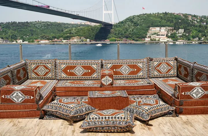 U-shaped floor sofa set in rust brown with black and white kilim-pattern backrests, a square ottoman and floor pillows on a wood-look floor