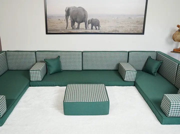 Wide view of a sage linen majlis running along three walls, with gingham back cushions around a white rug and ottoman