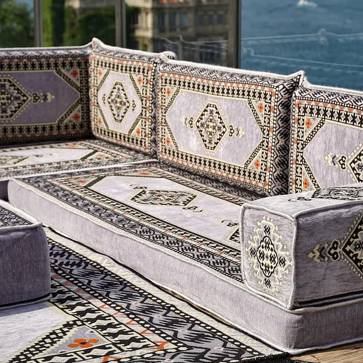 Close view of a light gray medallion corner showing a box armrest, the ottoman edge and a black and white kilim rug