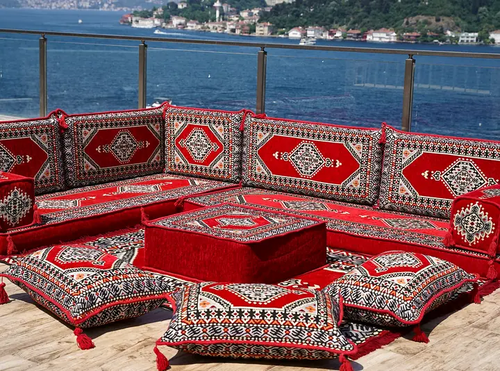 Red corner floor sofa with gray-framed medallions on every backrest, a red ottoman and tasseled floor pillows in front