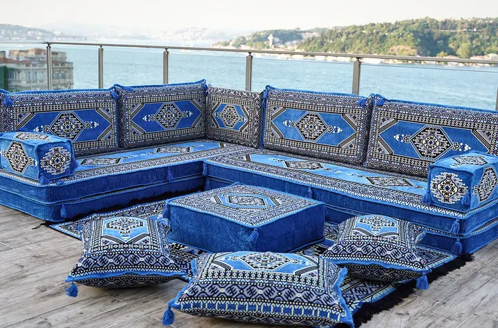 Royal blue L-shaped floor seating with patterned backrests, a royal blue ottoman and tasseled floor pillows before the seats