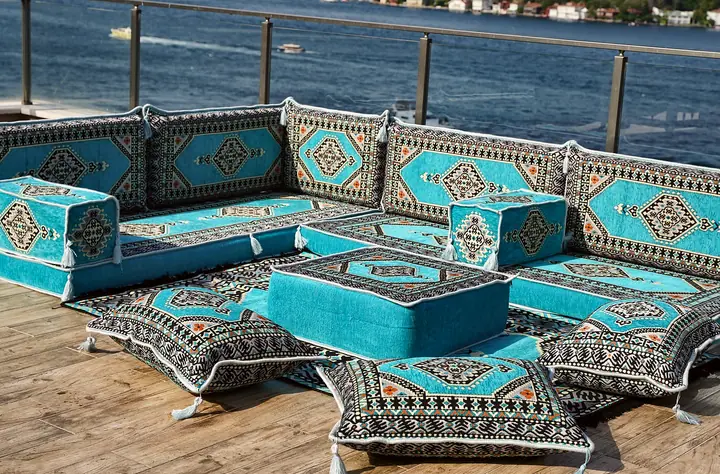Turquoise medallion floor seating turning a corner, with a turquoise ottoman and three tasseled floor pillows in front