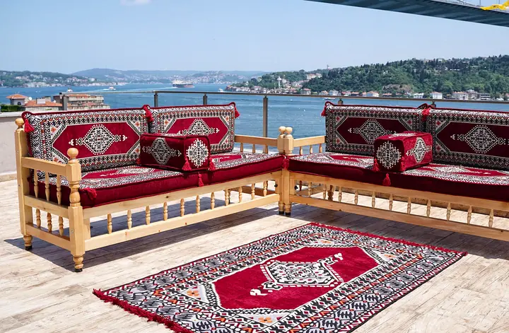 Maroon framed-medallion cushions on two wooden benches meeting at a corner, with armrest bolsters and a kilim-style rug