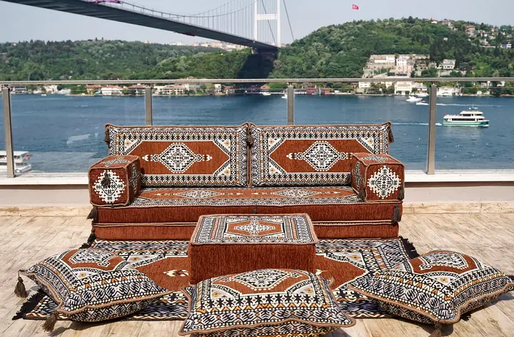 Rust brown medallion single floor sofa with two backrests, box armrests, an ottoman and three floor pillows on a terrace above the water