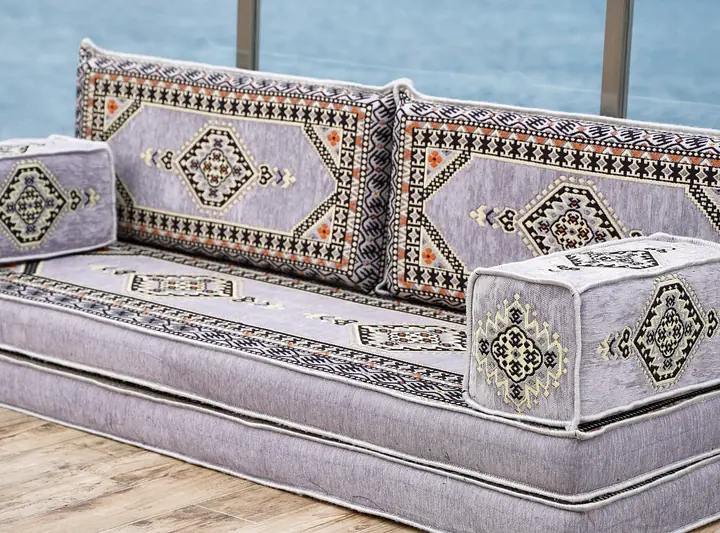 Three-quarter view of a light gray medallion floor couch with box armrests closing both ends of the seat
