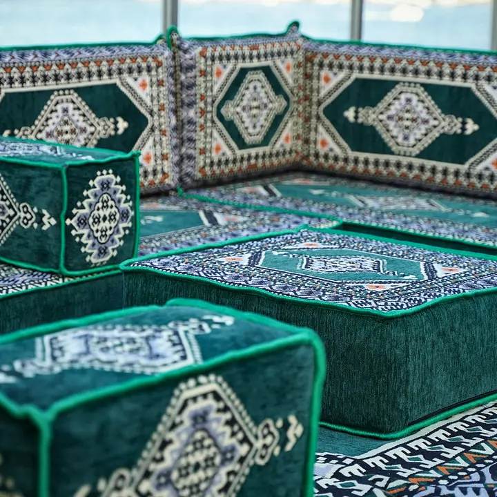 Low close view of a dark green medallion corner seat beside the ottoman and the edge of the matching rug