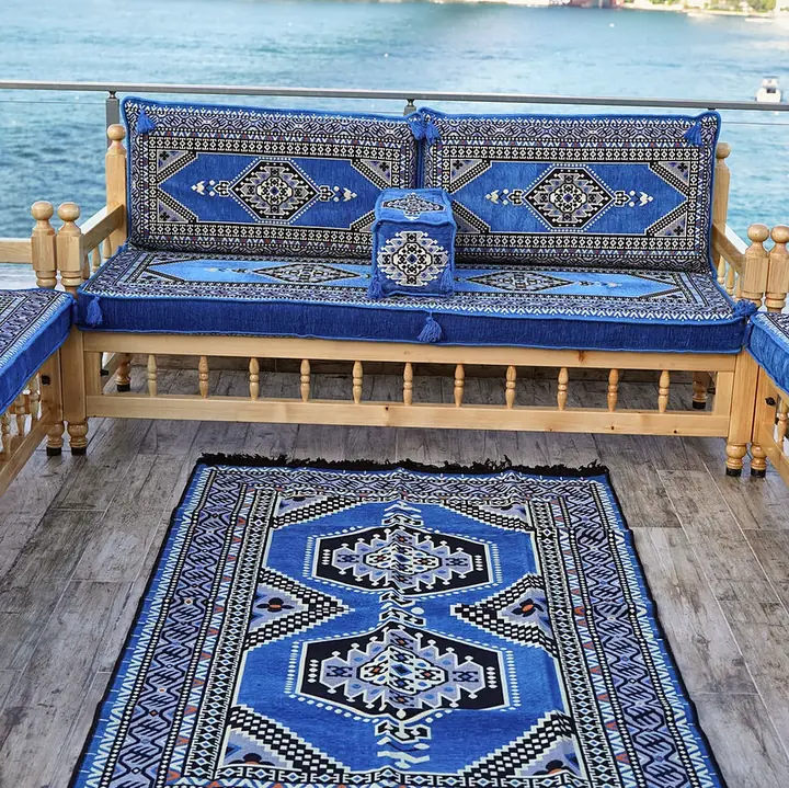 Pine bench with turned posts and blue medallion cushions facing a matching blue rug, with side benches closing in on a wooden deck