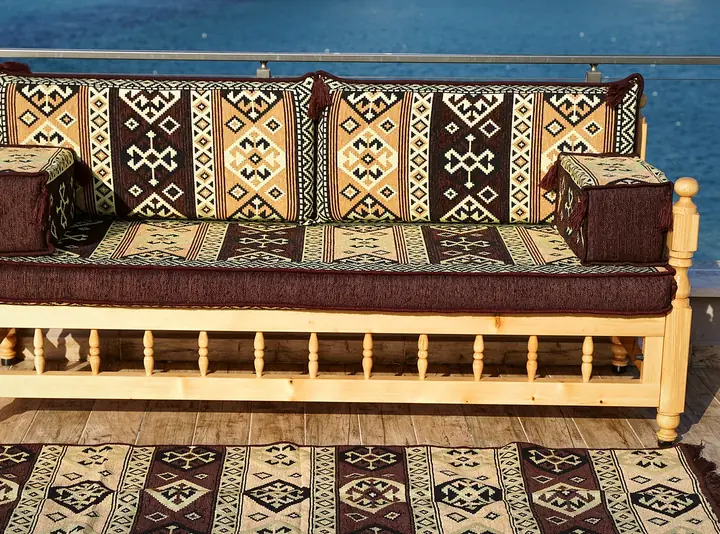 Single pine bench with a brown and cream kilim-pattern seat cushion, two backrests and armrest bolsters, a matching rug in front