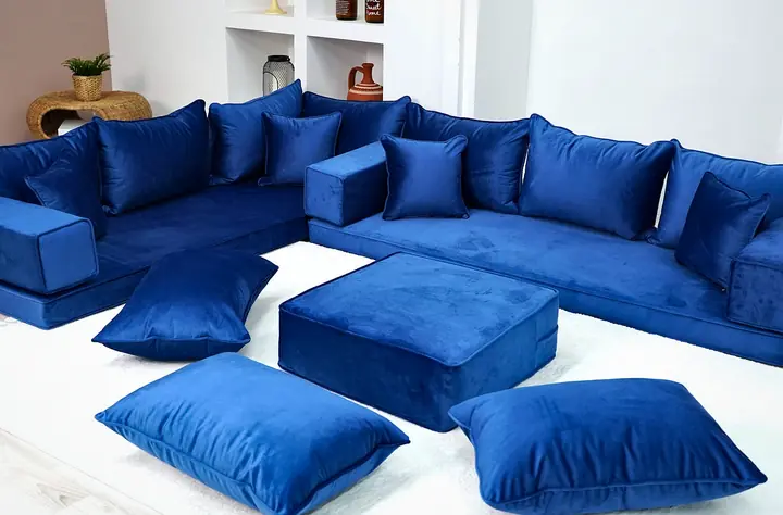 Royal blue velvet corner set with square backrests and small throw pillows, a blue ottoman and floor pillows in front