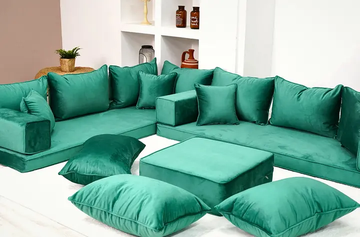 Emerald green velvet floor seating turning a corner, with a square green ottoman and three floor pillows on a white rug