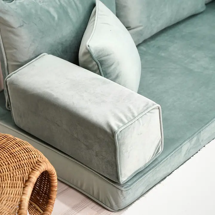 Close view of a seafoam velvet block armrest against a square backrest pillow, with a rattan basket at the lower edge