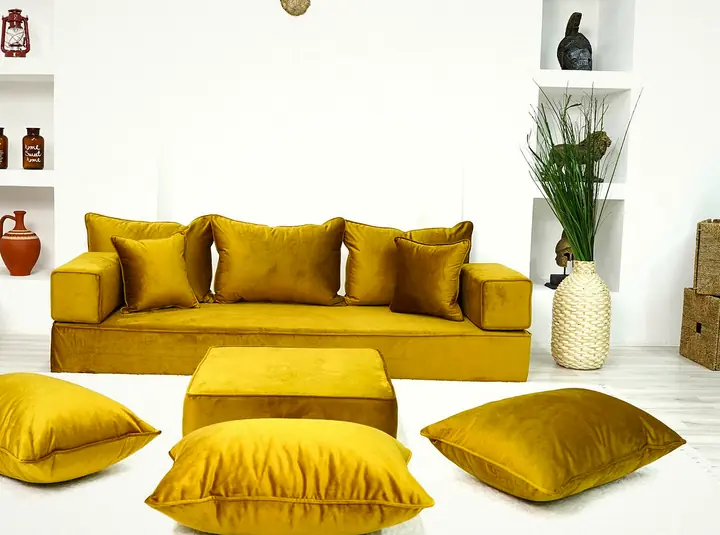 Gold velvet floor couch along one wall with thick square backrests, a gold ottoman and three plump floor pillows