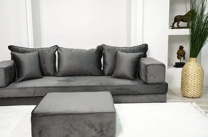Charcoal gray velvet single floor sofa with square backrests and block armrests, a large gray ottoman on a white rug