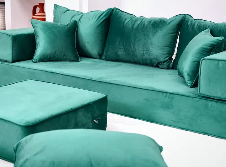 Close view of an emerald green velvet floor seat with block armrests, square backrests and a green ottoman in front