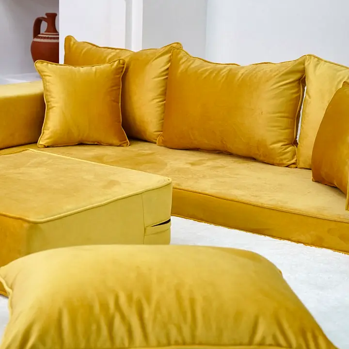 Close angle on a mustard velvet seat corner with a block armrest, a throw pillow, the ottoman and floor pillows