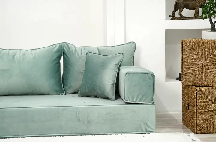 Seafoam green velvet seat with square backrests and a block armrest beside two stacked woven storage cubes
