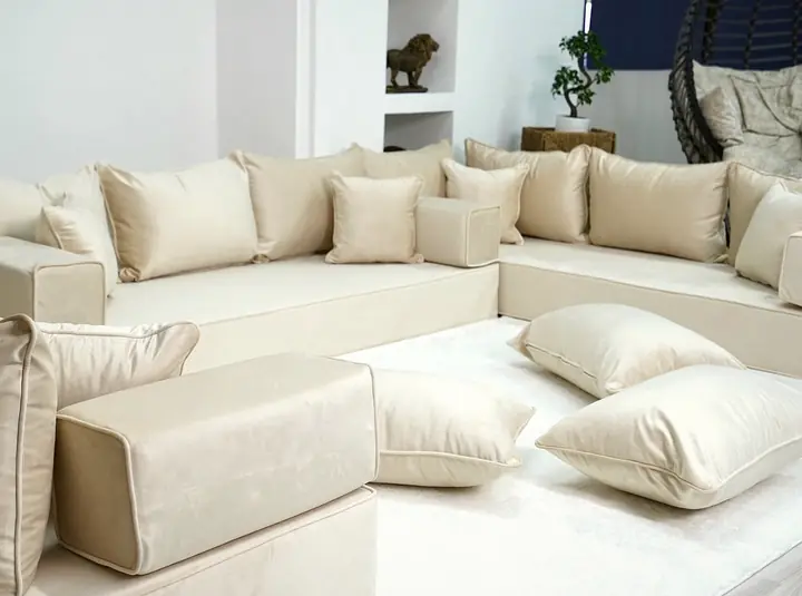 Cream velvet U set seen from one corner, with square backrest pillows, small throw pillows and floor pillows on a white rug