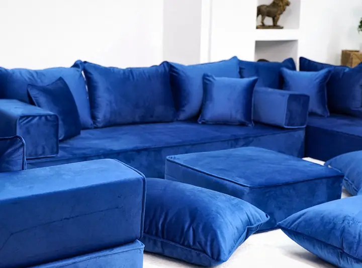 Close view of a thick royal blue velvet majlis with square backrests, a blue ottoman and floor pillows in front