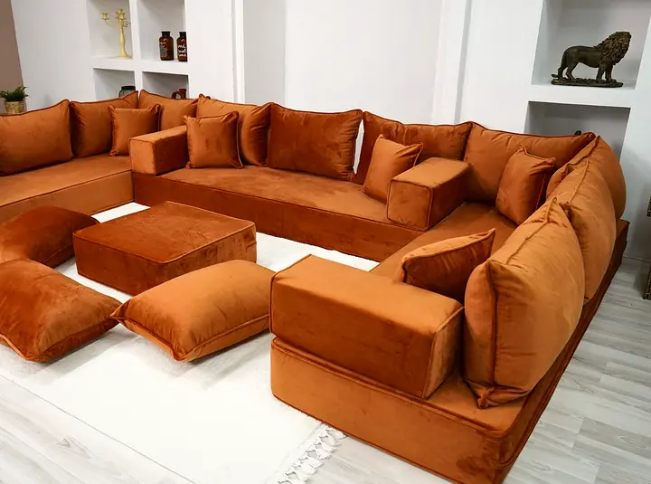 Brick red velvet floor seating on three walls with thick seats, block armrests, an ottoman and floor pillows
