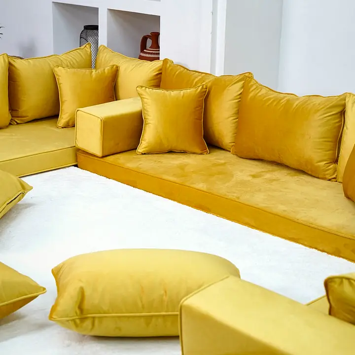 Close angle on mustard velvet seats with a block armrest and plump floor pillows resting on a white rug