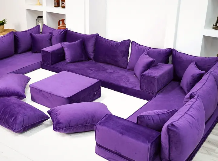 Purple velvet U-shaped floor sofa with square backrests, a purple ottoman and three floor cushions, seen from a high angle