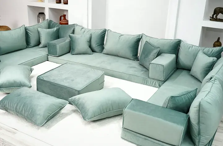 Seafoam green velvet floor seating around three walls, seen from above with its ottoman and floor pillows in the middle