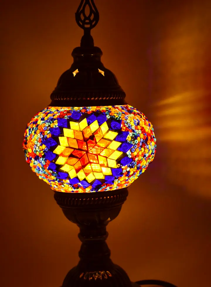Multicolor star-pattern glass mosaic table lamp on a bronze-tone base, lit against an amber backdrop