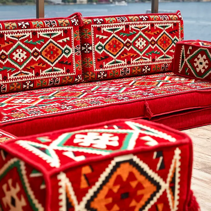 Close view of a red kilim armrest bolster with the hooked diamond pattern of the backrests behind it