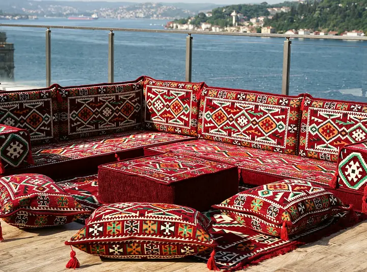Deep red kilim floor couch turning a corner, with an ottoman and floor pillows set inside the L