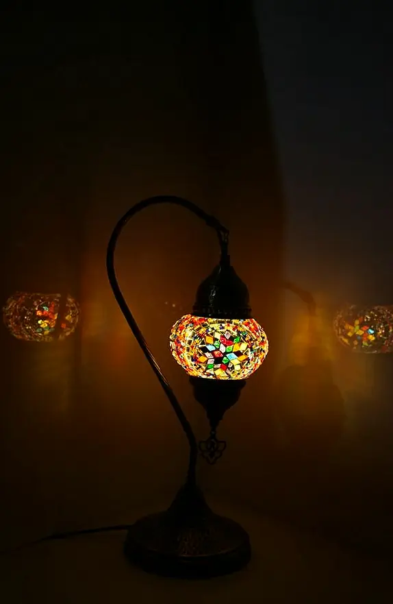 Swan-neck glass table lamp switched on in a dark room, throwing amber patterns of light around it