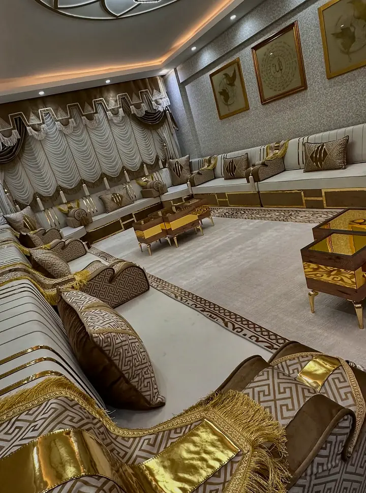 Angled view of the ivory and mocha majlis with a fringed Greek-key armrest throw in front and gold-glass tables in the middle