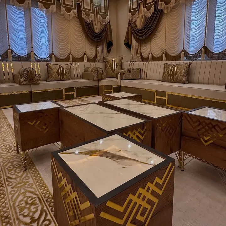 Close-up of a wood-grain side table with a gold lattice inlay, a white marble-look top and gold legs beside the cream majlis