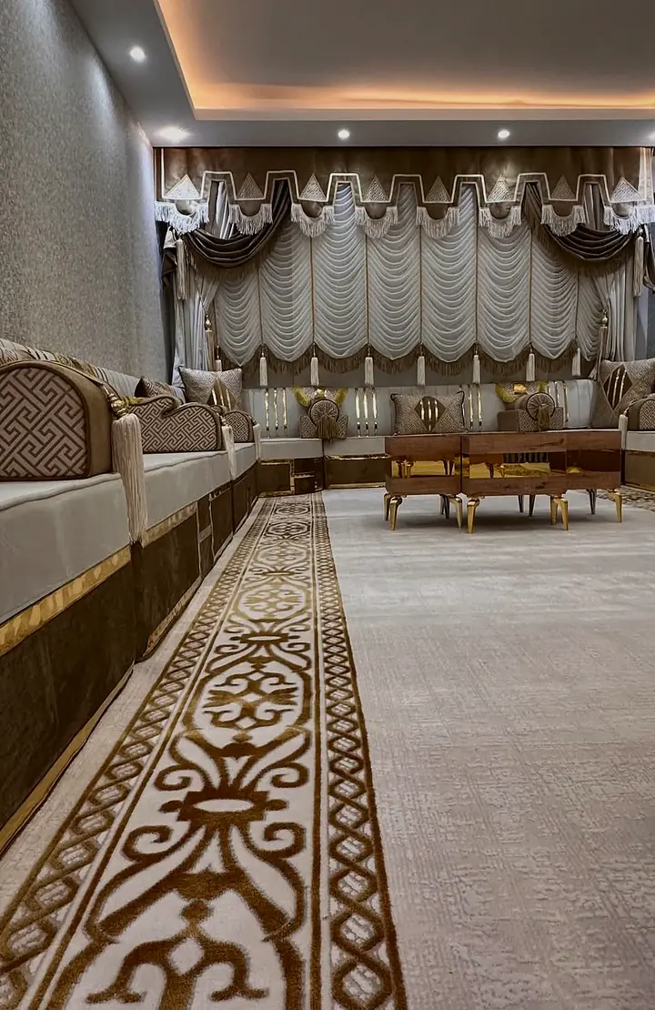 Long run of ivory seating on a mocha base with gold bands, leading to stepped valances, with an arabesque runner rug down the room
