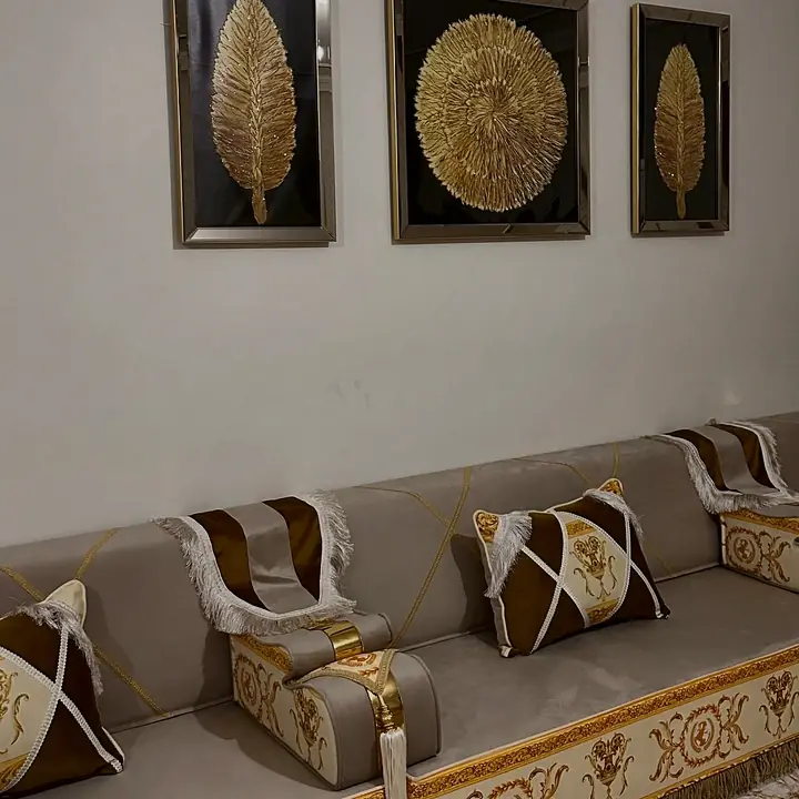 Taupe seating section with brown and ivory cross pillows below three framed gold-leaf panels on a pale wall