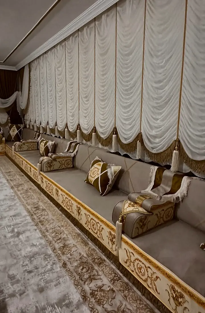 Taupe velvet seats and backrests with thin gold piping, cross-pattern pillows and tasseled bolsters along a curtained wall