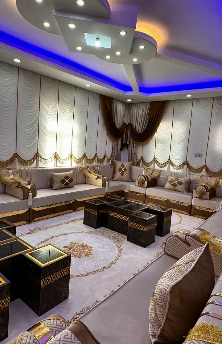 Taupe velvet majlis seen from one end, with chocolate and cream diamond pillows, gold base strips and nesting tables in the middle