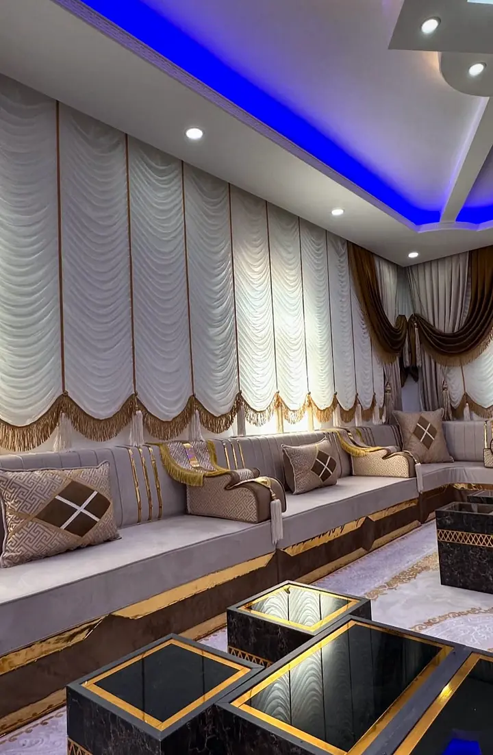 Low view of dark marble-look nesting tables with gold lattice bands in front of taupe seating and a diamond-pattern pillow
