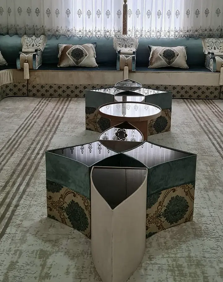 Teal and cream majlis on three walls with diamond-patterned cushions below embroidered sheers, gray and teal drapes and petal-shaped tables