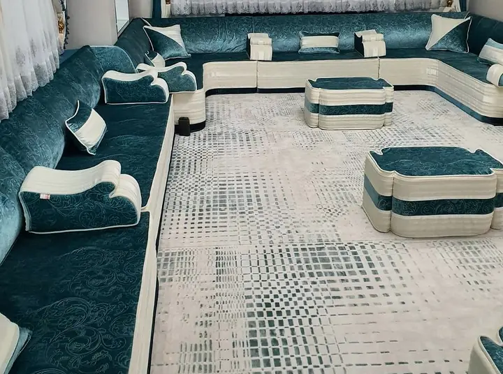 Teal crushed-velvet floor majlis with ivory piping, teal-banded poufs and a grid-pattern rug in a low lounge corner