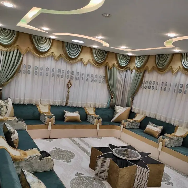 Teal velvet U-shaped majlis with cream and gold trim, a star-shaped table on an ivory medallion rug and sage swag curtains with gold fringe