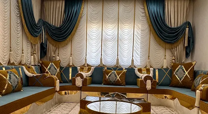 U-shaped majlis in teal and mustard velvet with gold trim, two fringed star tables in the middle and white swag curtains