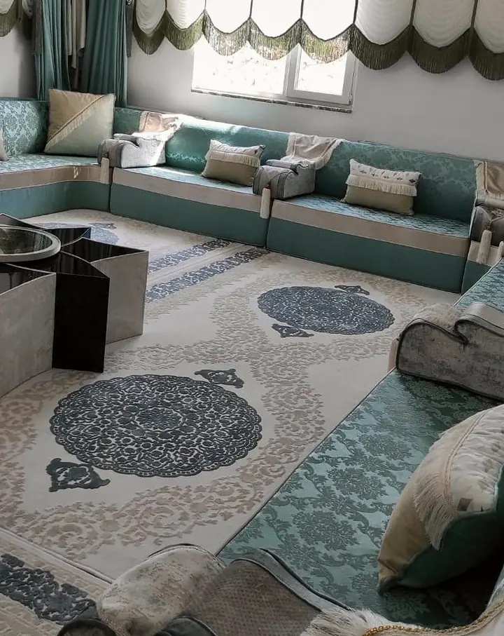Teal and sage majlis along two walls beneath white scalloped blinds and teal curtains, with a star-shaped table on a cream medallion rug