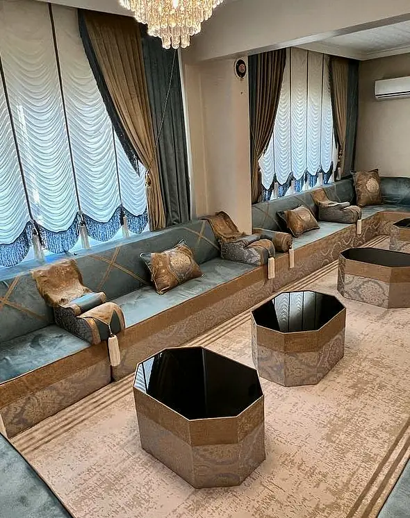 Blue-gray velvet majlis on three walls with gold cross bands, damask cushions and octagonal tables under crystal chandeliers